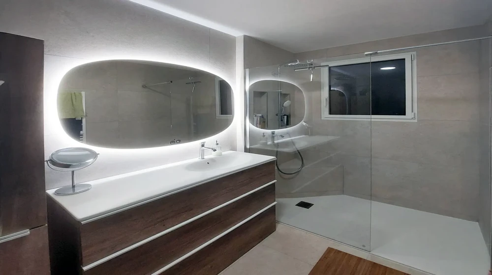 Salle de bain moderne avec douche à l'italienne, meuble vasque suspendu en bois foncé, plan de travail blanc, miroir ovale rétroéclairé LED