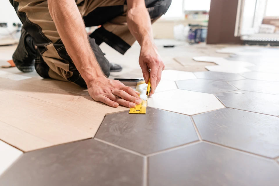 Ouvrier carreleur professionnel installant du carrelage dans une pièce en rénovation, utilisant une ventouse de pose pour positionner les carreaux blancs