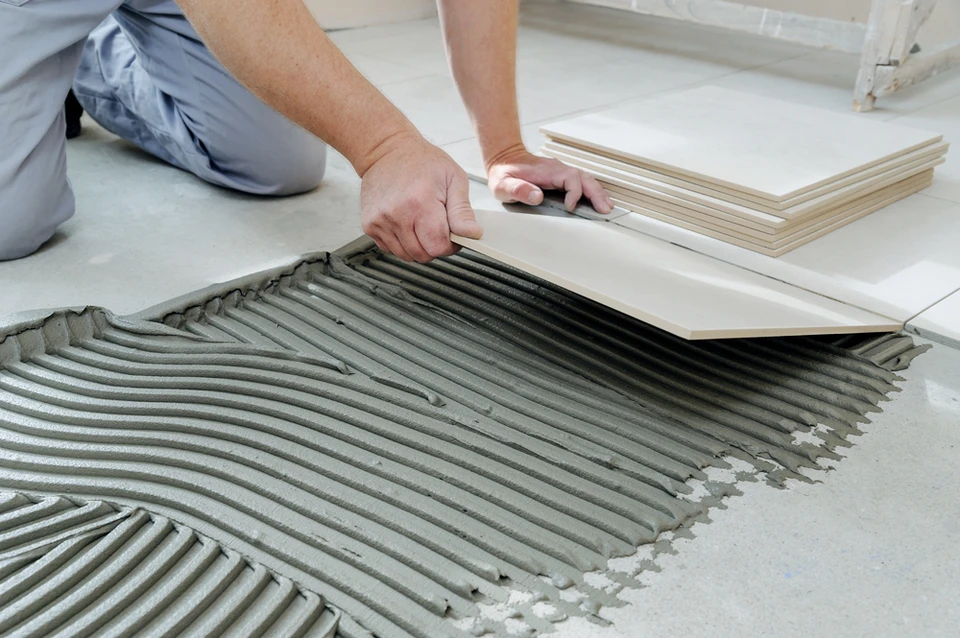 Ouvrier en &eacute;quipement de protection individuelle utilisant une carrelette manuelle pour d&eacute;couper du carrelage sur chantier de construction